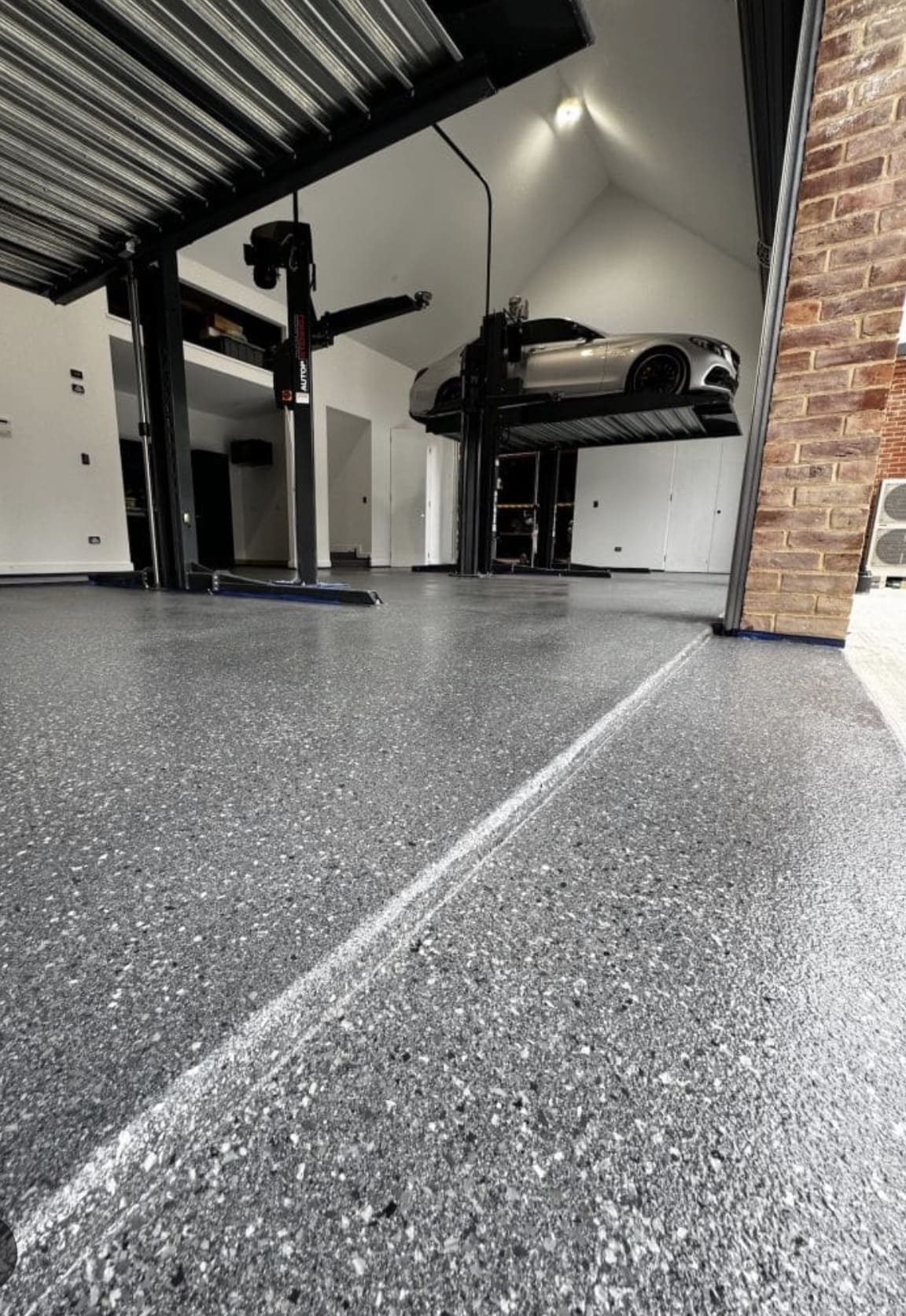Grey flake epoxy garage floor with a luxury car on a lift, Titan Floor Systems